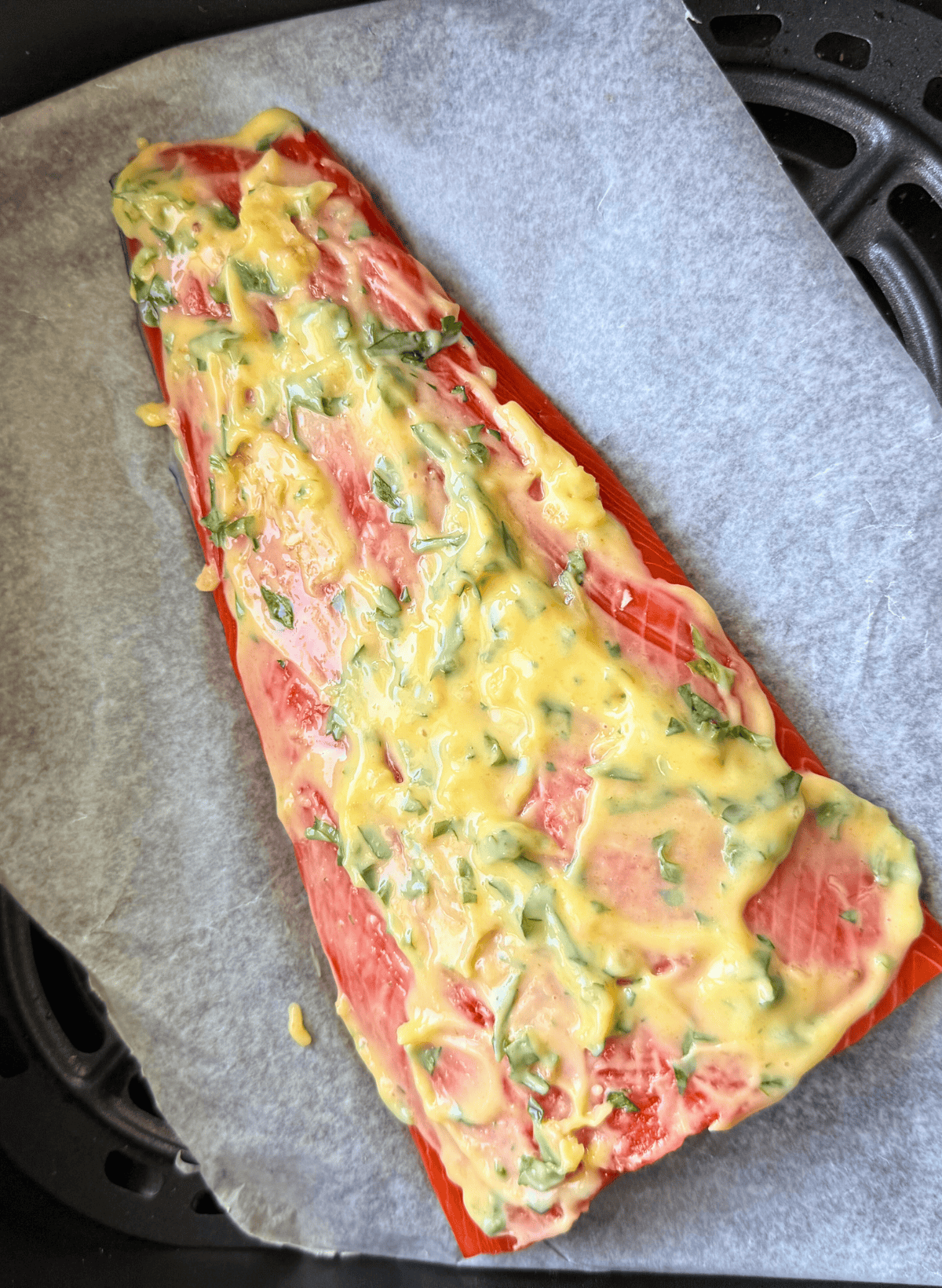 raw filet of sockeye salmon with garlic butter on parchment paper in an black air fryer basket