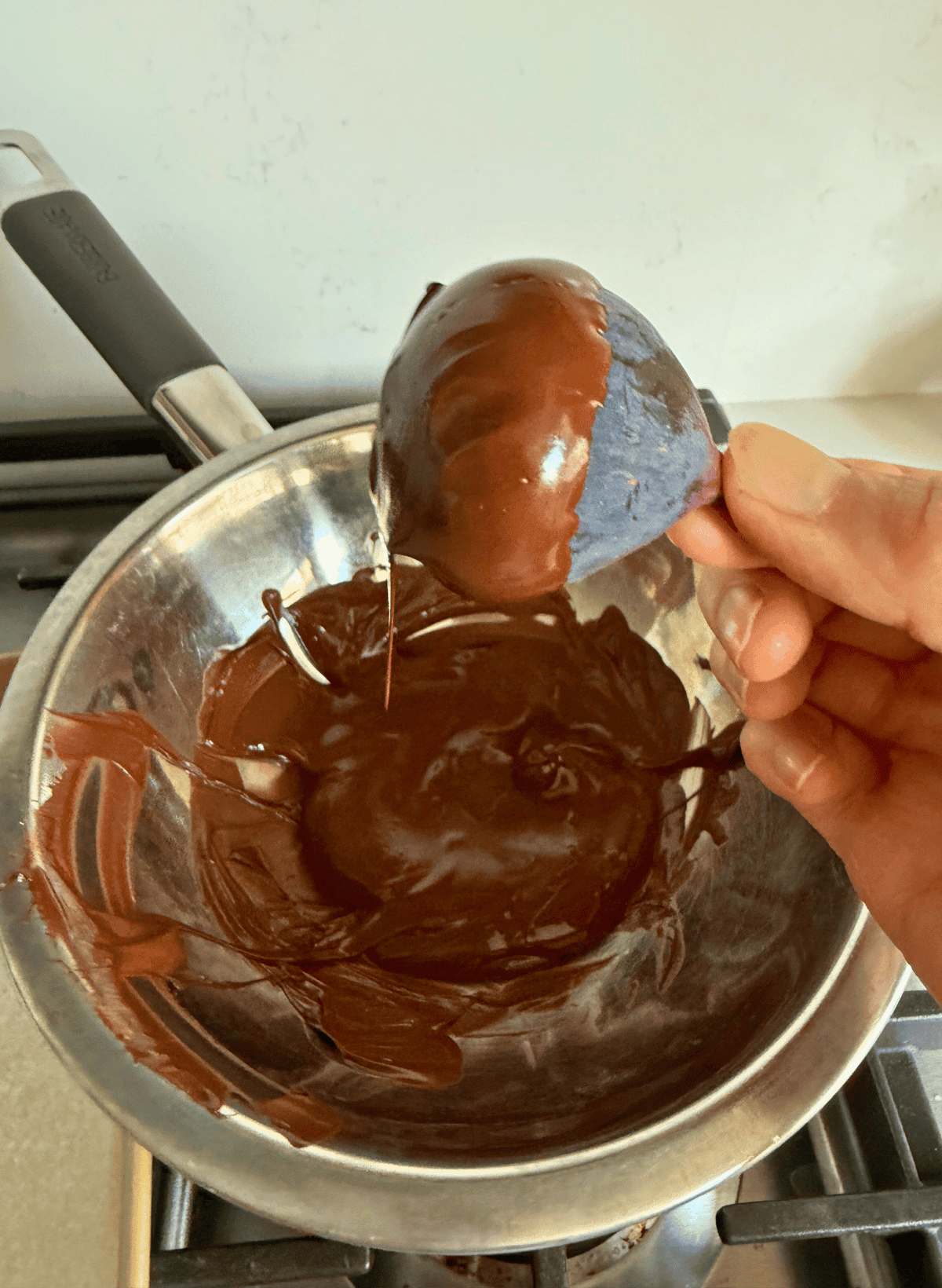 hand holding a chocolate dipped fig over a silver bowl of melted chocolate
