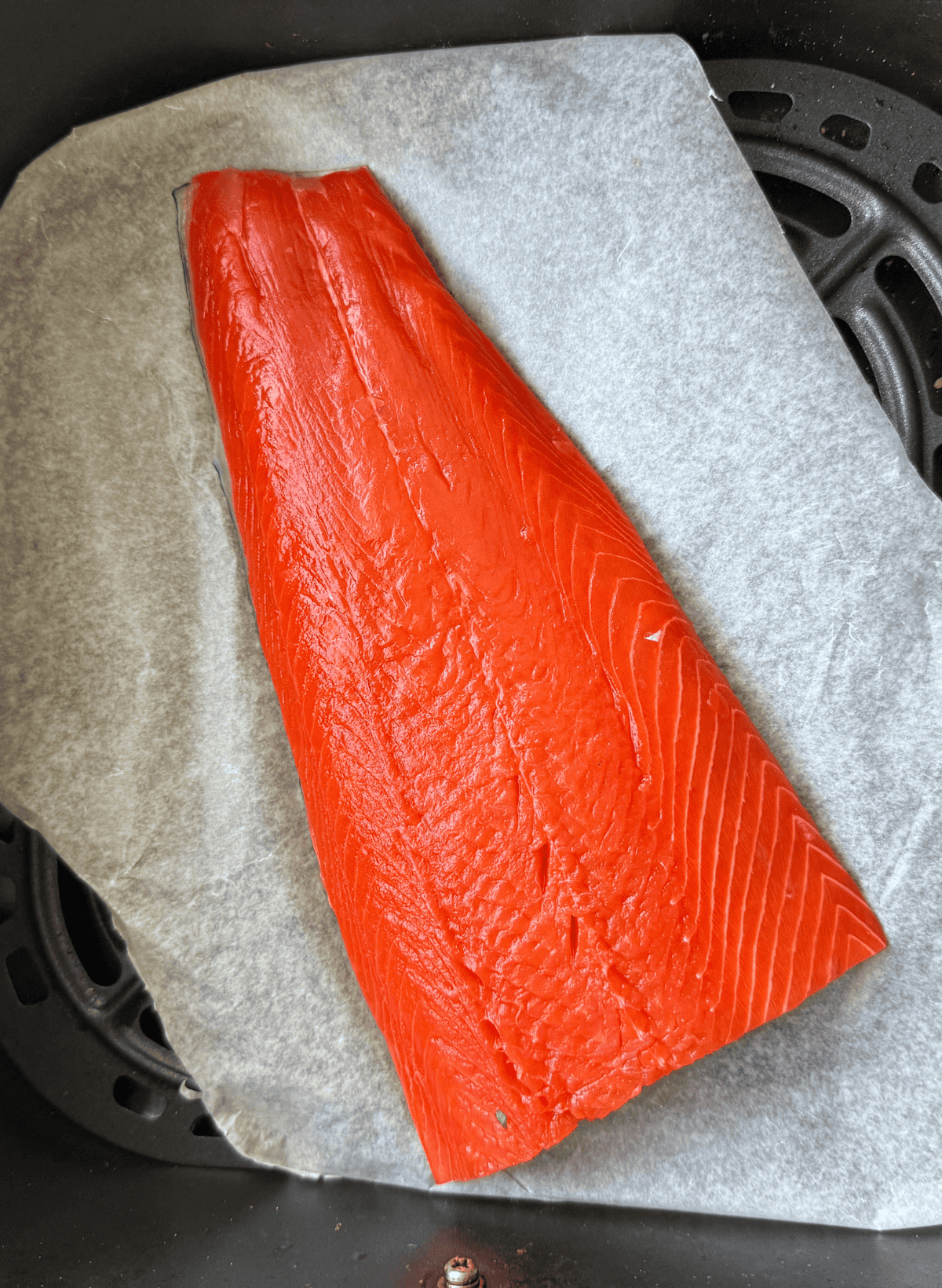 raw filet of sockeye salmon on parchment paper in an black air fryer basket