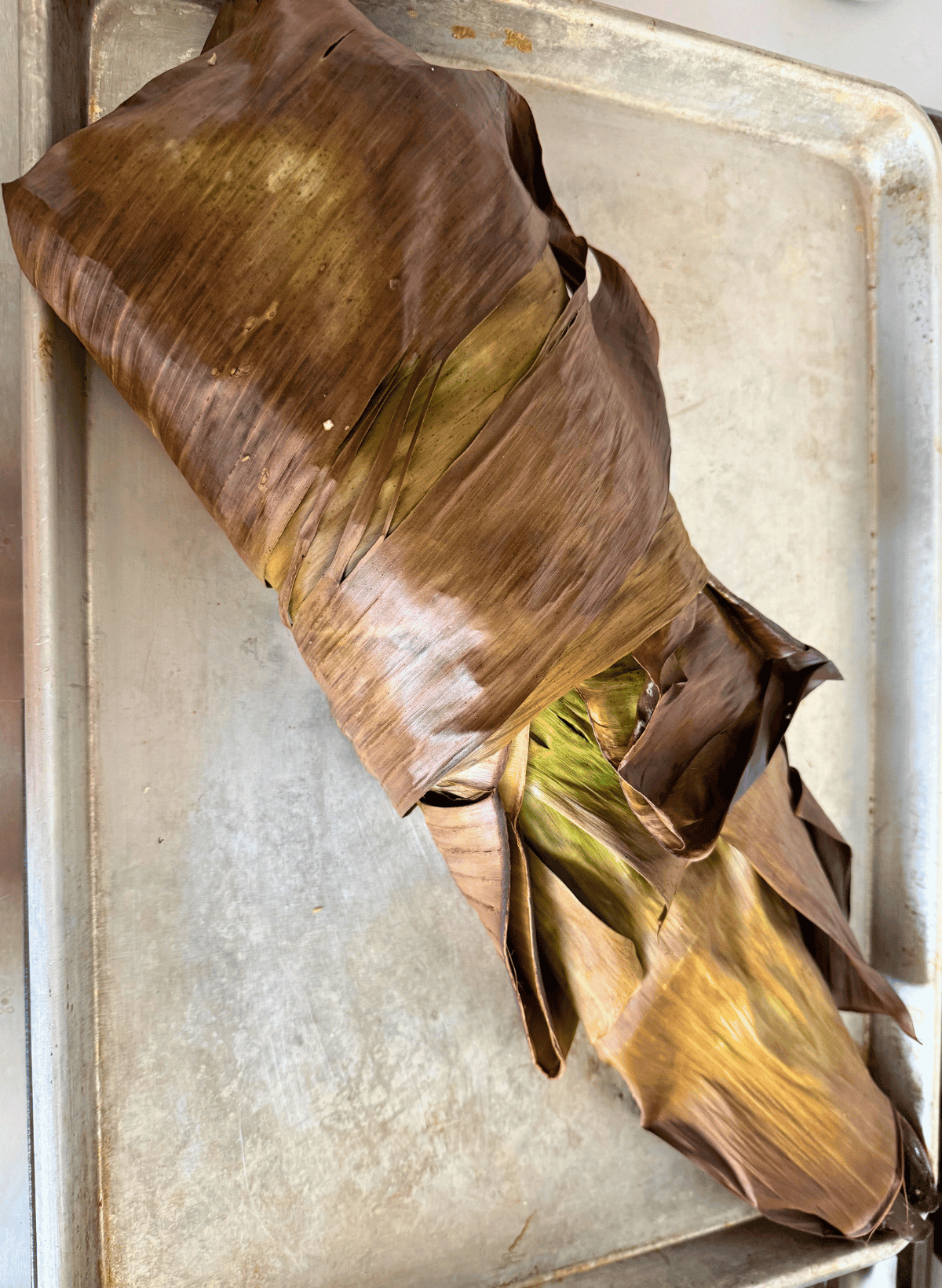 cooked banana leaf wrapped coho salmon on a sheet pan