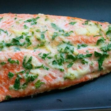 Sockeye salmon with garlic butter on a black plate with lemon wedges