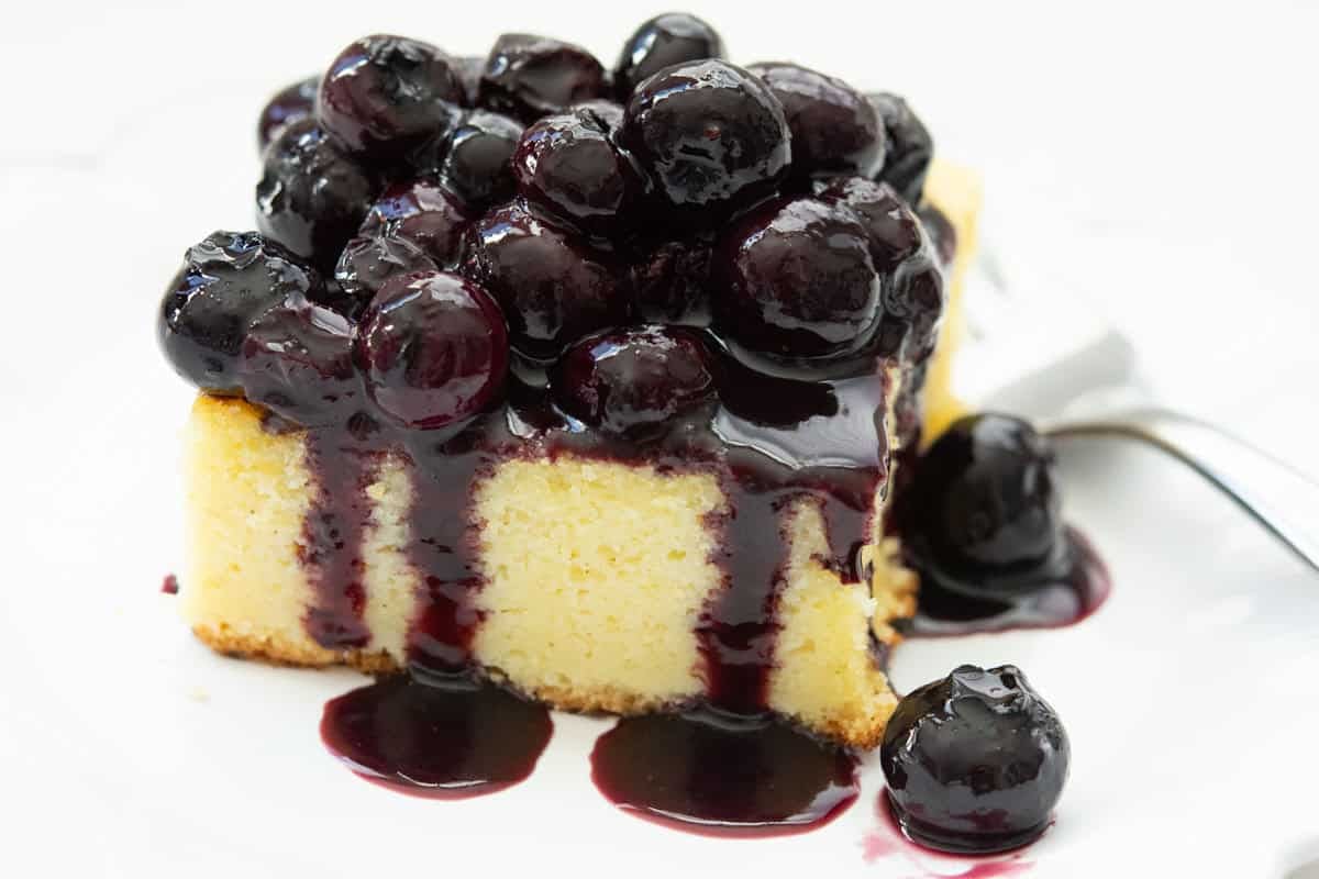 Blueberry sauce on a cornmeal cake with a fork on a white plate