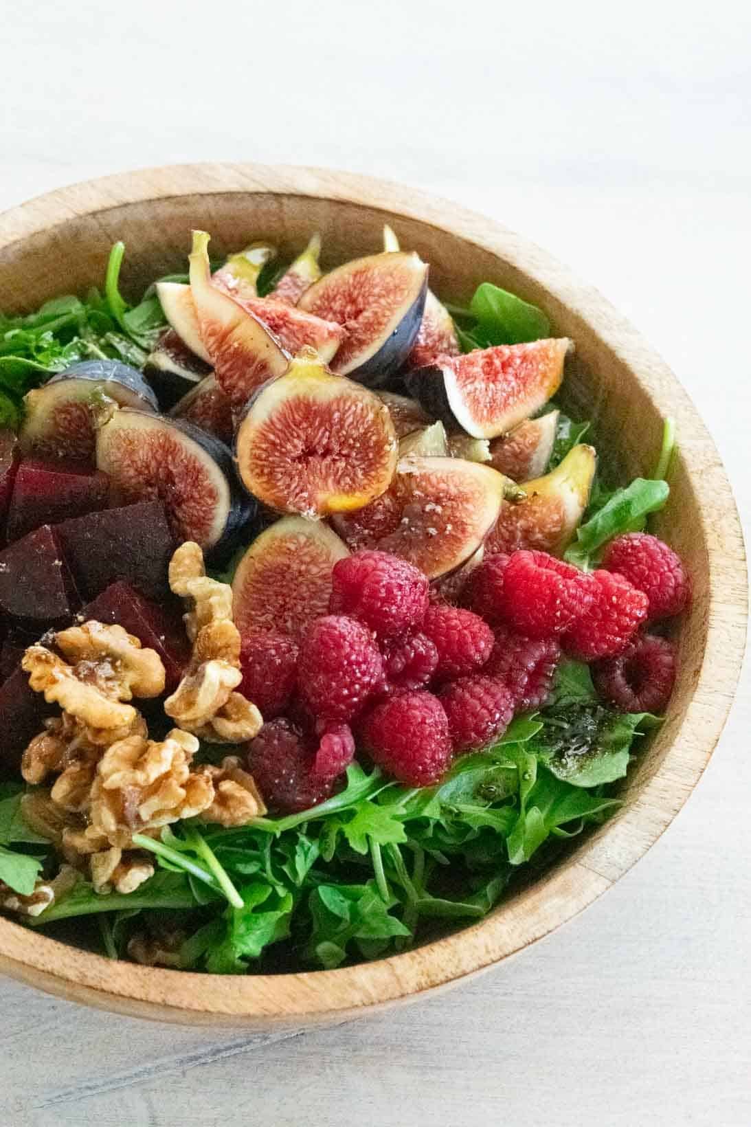 fig and beet salad with raspberries and arugula in a brown wooden bowl