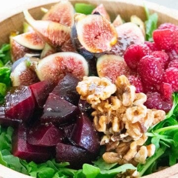 fig and beet salad with raspberries and arugula in a brown wooden bowl