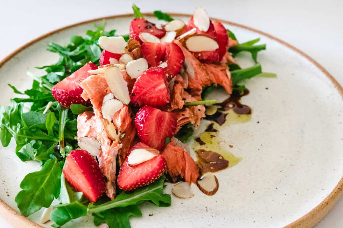 Sockeye salmon and strawberry salad on a white plate with sliced almonds