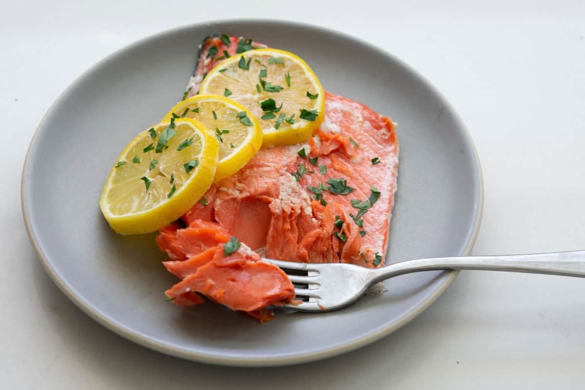 forkful of slow roasted sockeye salmon with sliced lemons on a round gray plate