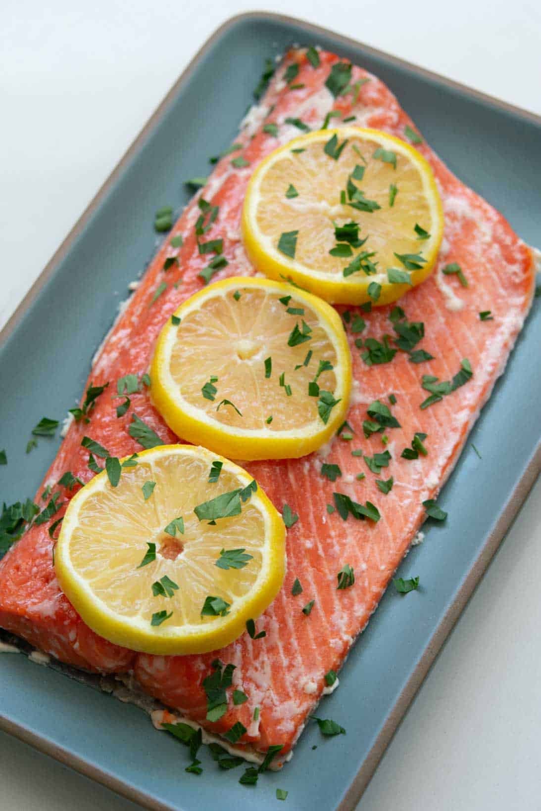 Slow roasted sockeye salmon with sliced lemons on a blue rectangular plate