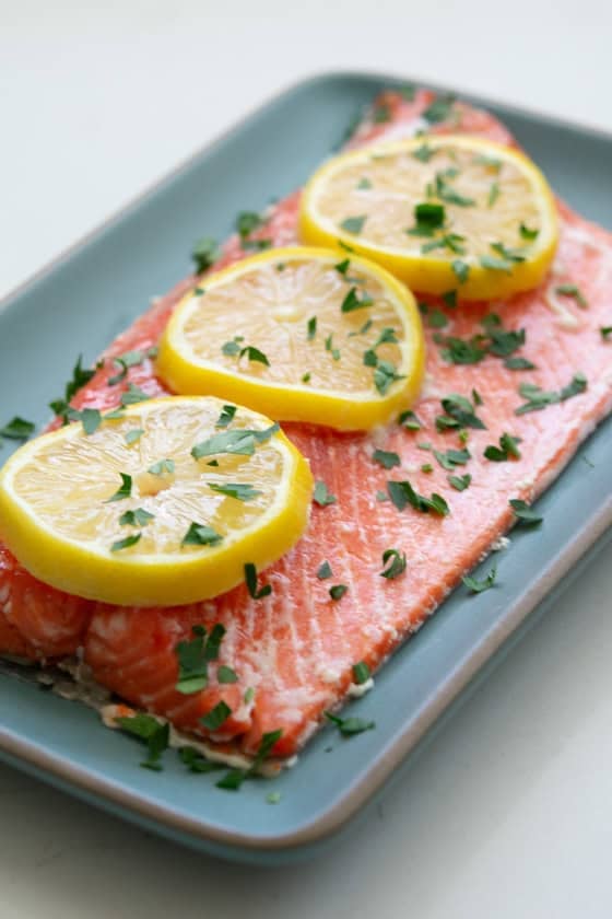 Slow roasted sockeye salmon with sliced lemons on a blue rectangular plate