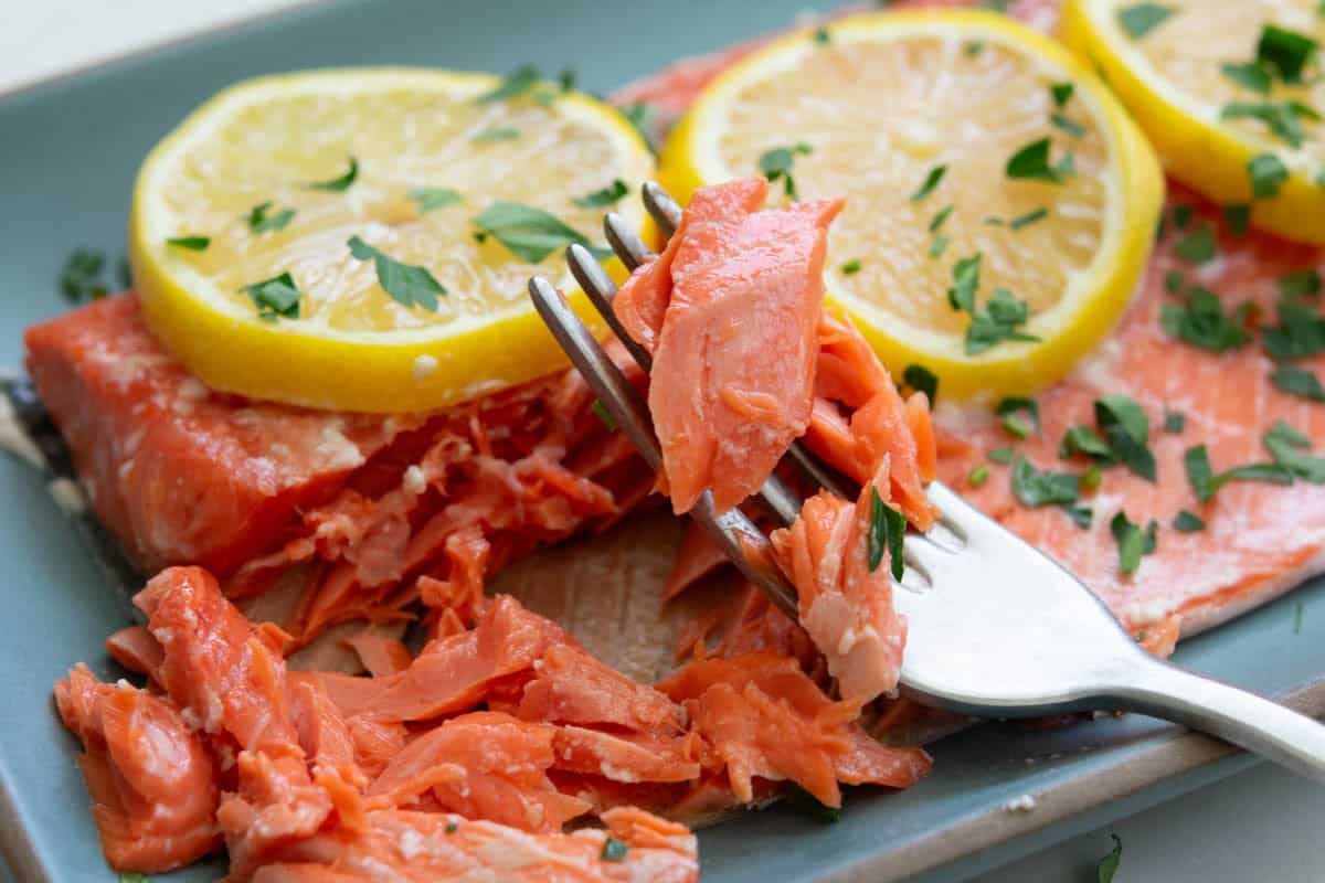 Slow roasted sockeye salmon with sliced lemons on a blue rectangular plate and a fork