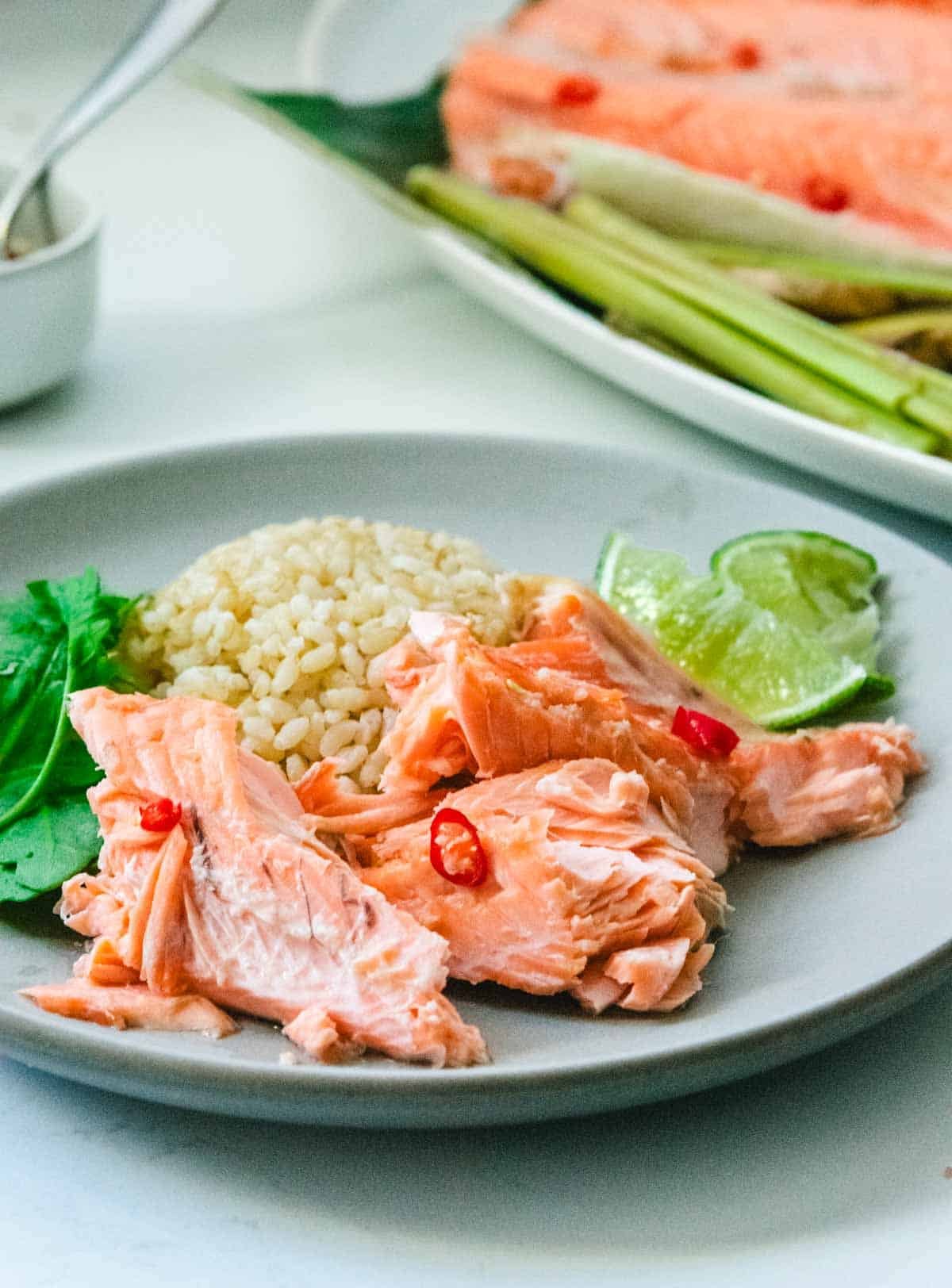 Chunks of cooked Coho salmon with brown rice, arugula leaves, and lime wedges on a round grey plate