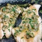 2 filets of sauteed rockfish with caper butter sauce in a black nonstick pan