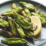 air fried shishito peppers with a lemon wedge on a round dark blue plate