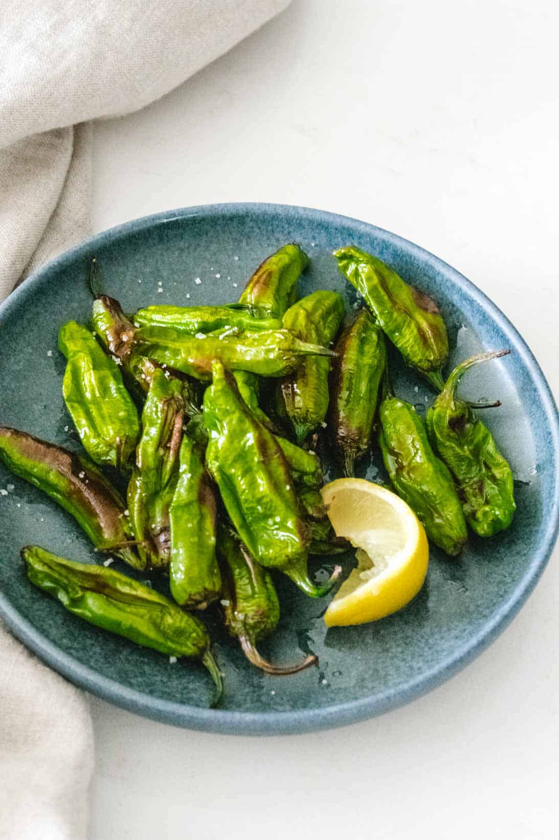 air fried shishito peppers with a lemon wedge on a round dark blue plate