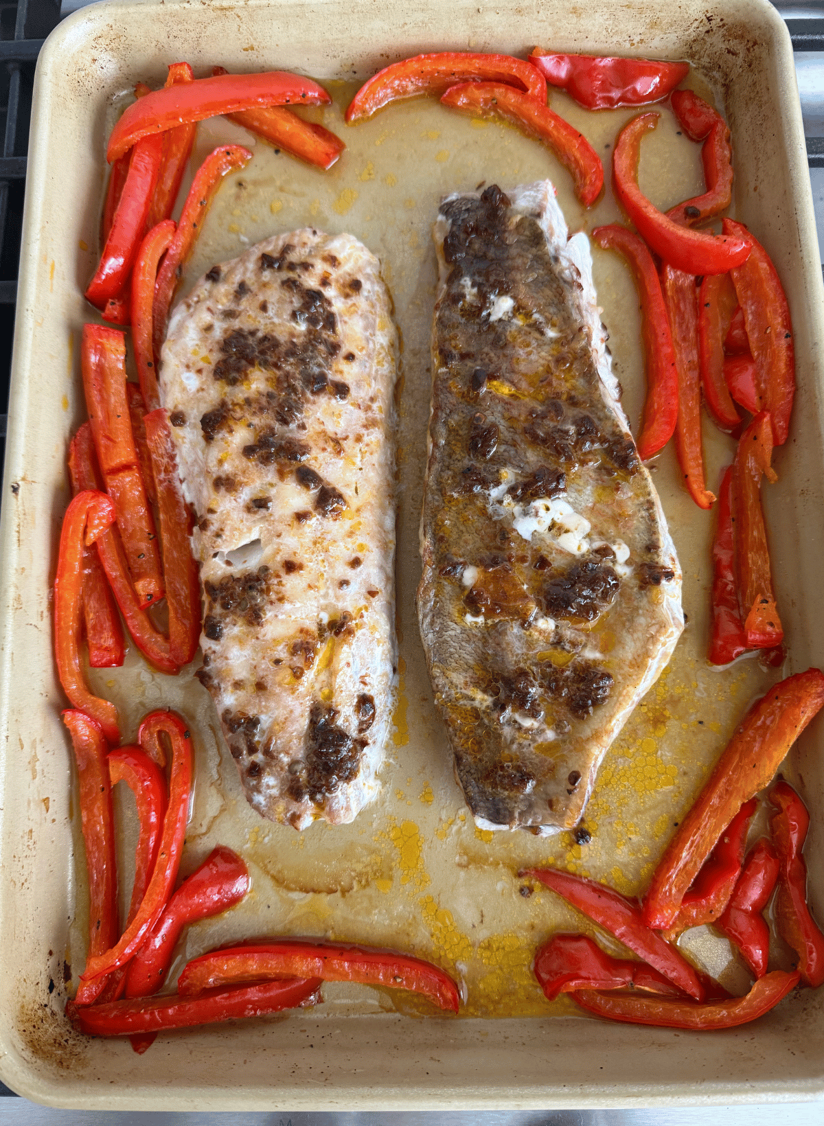 cooked chili pepper rockfish on a gold sheet pan with red bell pepper strips
