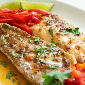 Chili pepper rockfish on top of mashed potatoes with red bell pepper strips and lime wedge on the side