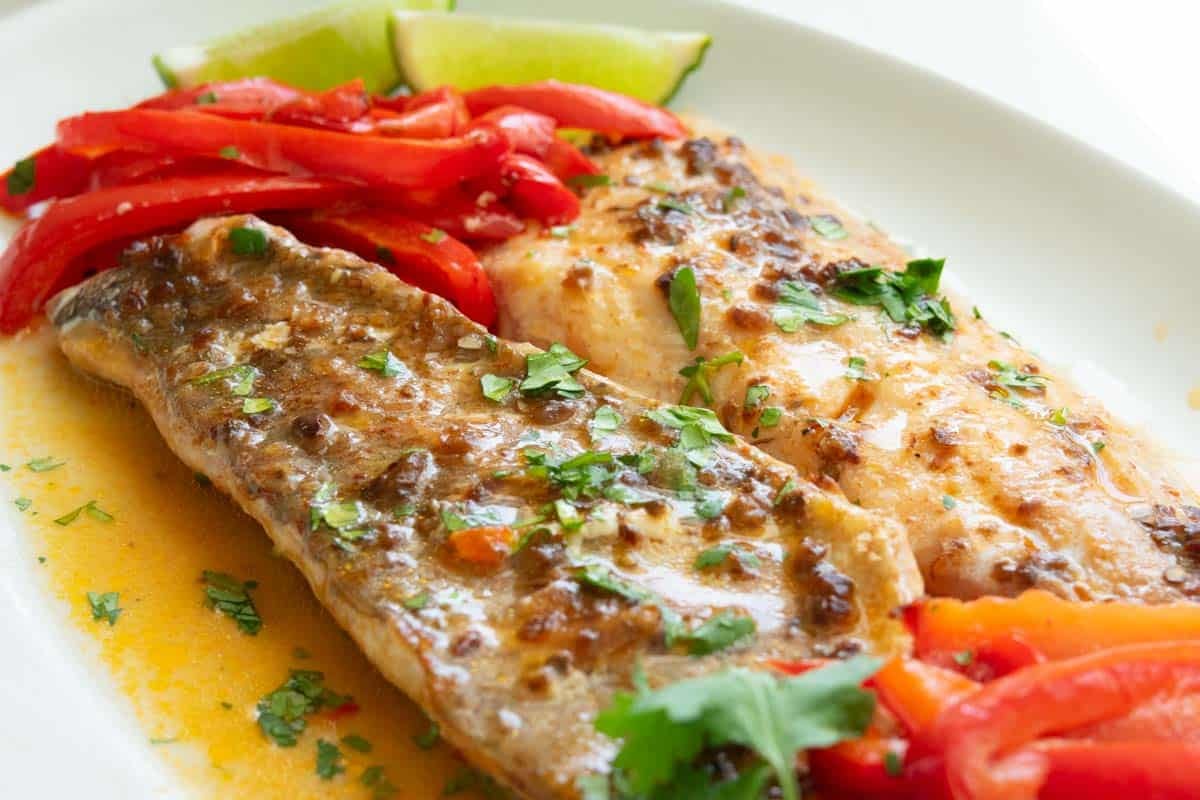 Chili pepper rockfish on top of mashed potatoes with red bell pepper strips and lime wedge on the side