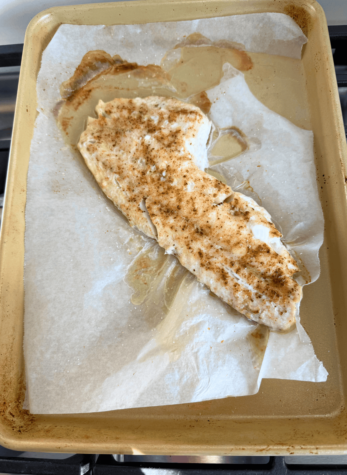 cooked rockfish fillet with seasoning on a parchment lined baking sheet