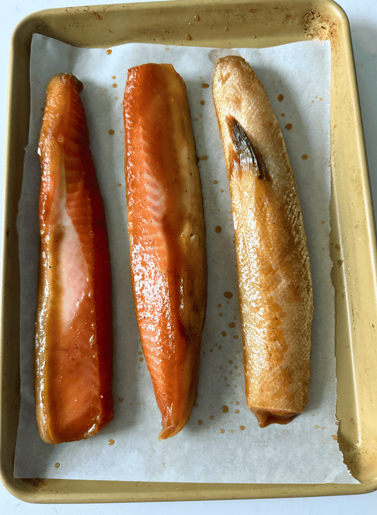 3 raw, marinated salmon bellies on a parchment lined gold baking sheet