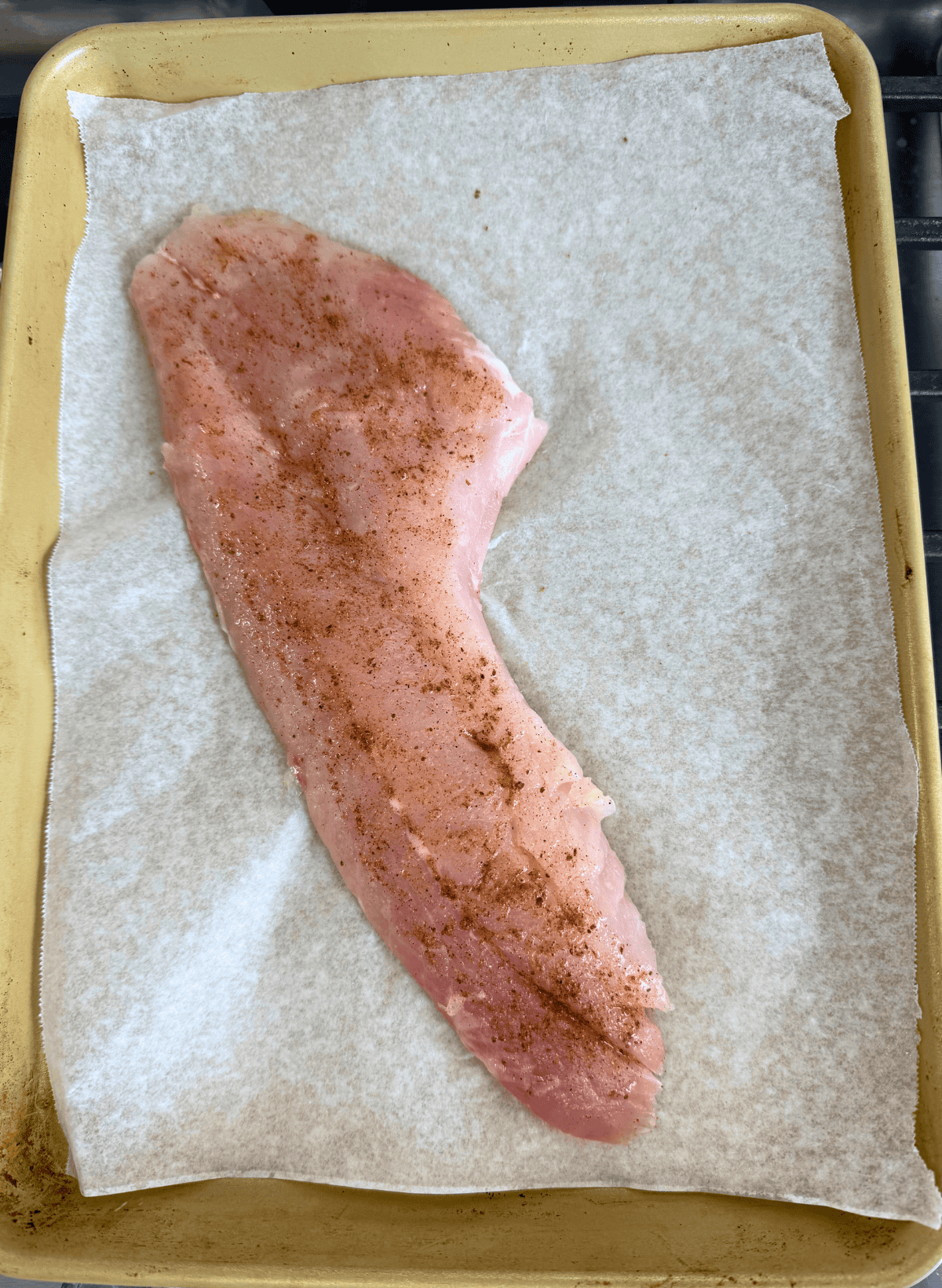 rockfish fillet with old bay seasoning on a parchment lined gold baking sheet