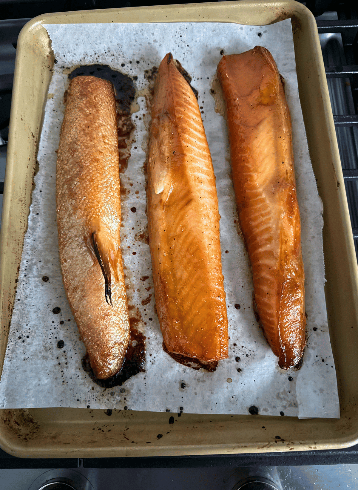 3 cooked salmon bellies on a parchment lined gold baking sheet