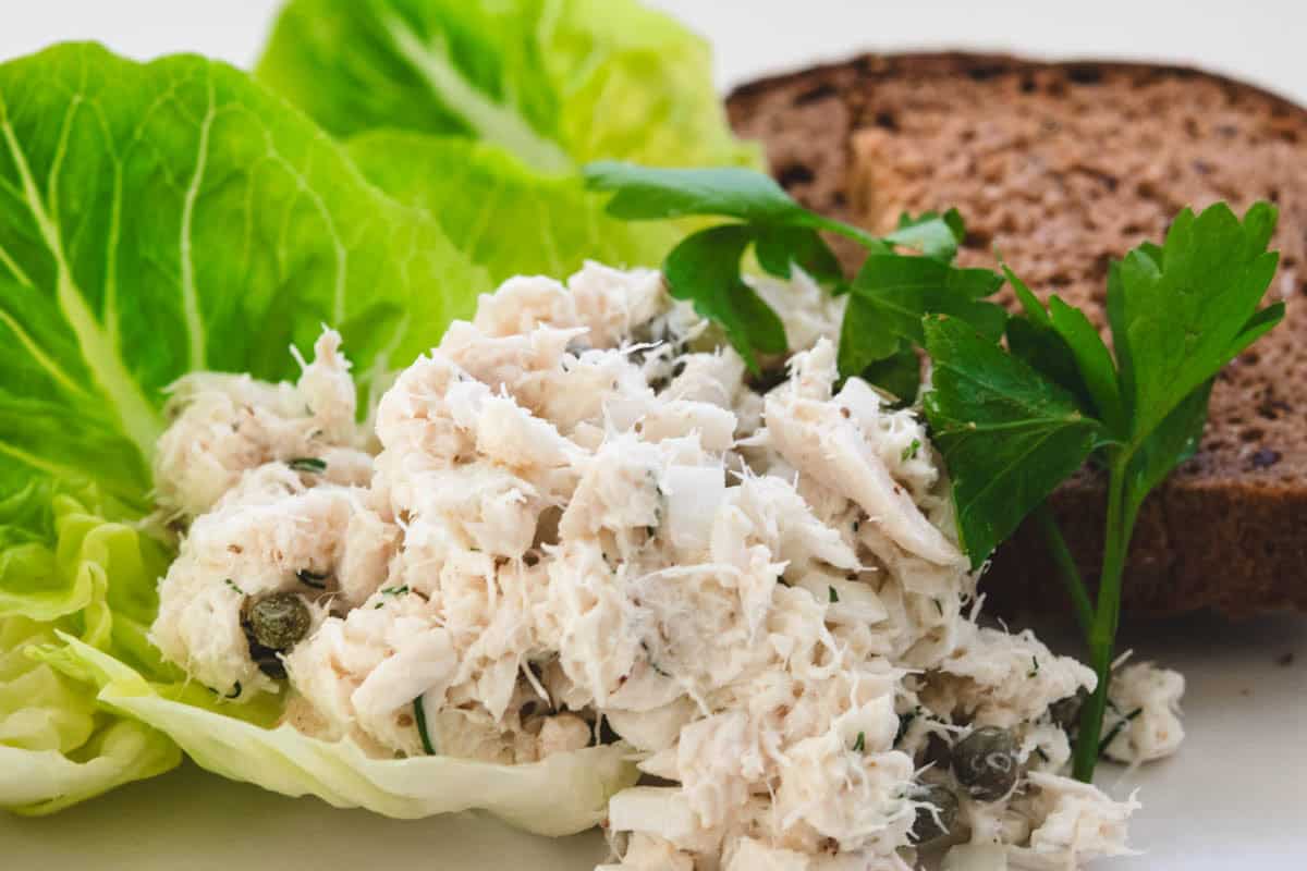 scoop of rockfish salad on lettuce leaves with a sprig of parsley and bread in the background