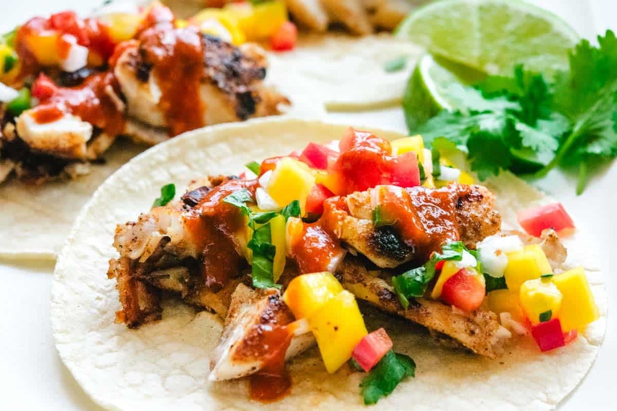 rockfish tacos with hot sauce with lime wedges and cilantro in the background