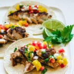 three rockfish tacos with lime wedges and cilantro in the background