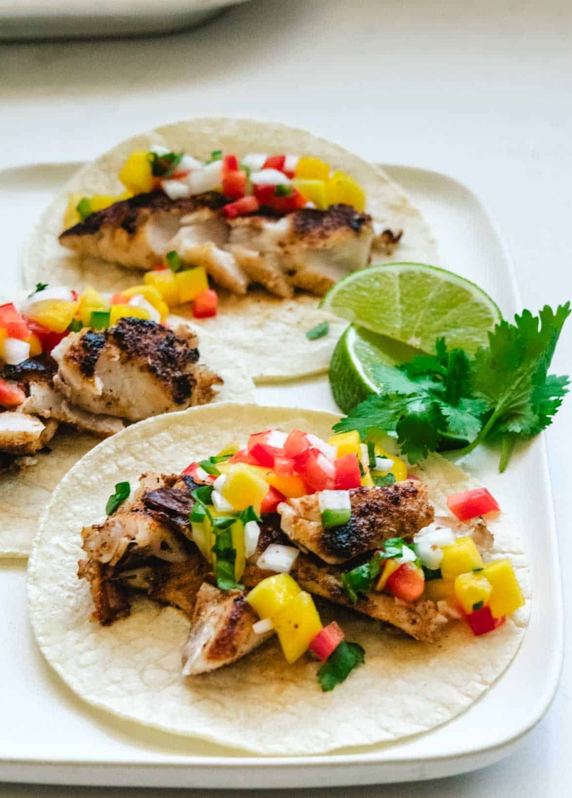 three rockfish tacos with lime wedges and cilantro in the background