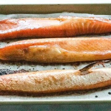 3 fillets of cookied salmon bellies on a parchment lined gold baking sheet