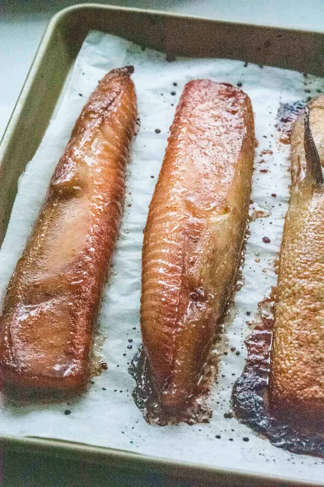 3 fillets of cookied salmon bellies on a parchment lined gold baking sheet