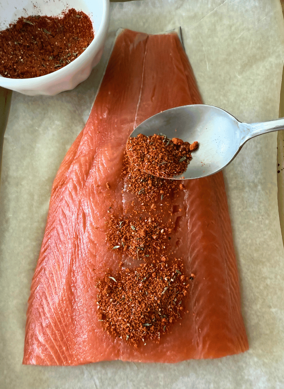 spoon spreading homemade trader joe's salmon rub on a fillet of coho salmon
