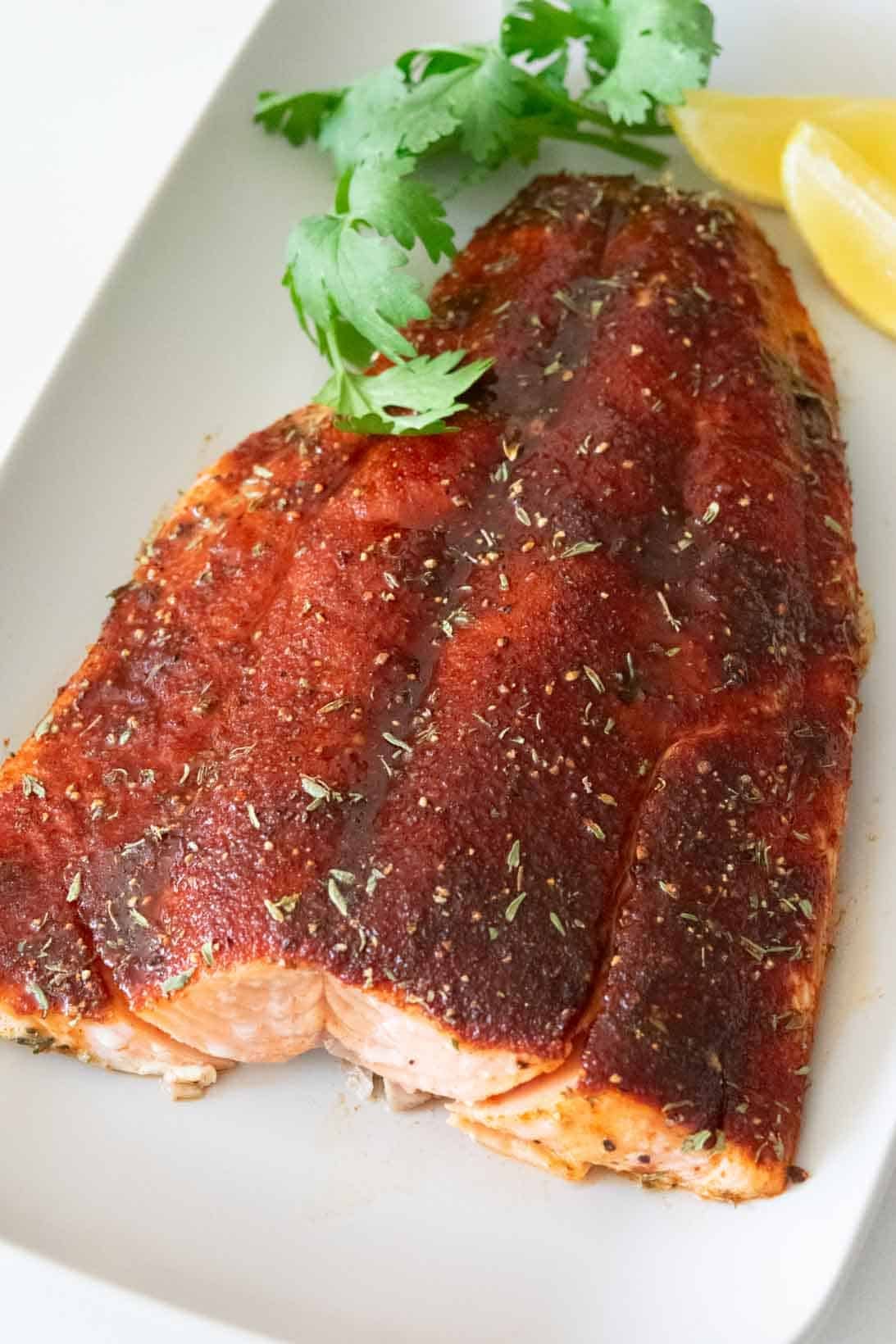 Baked Coho salmon fillet on a rectangular, gray plate with parsley sprigs and lemon wedges