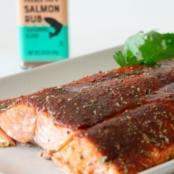 Baked Coho salmon fillet on a rectangular gray plate with parsley with trader joe's salmon rub bottle in the background