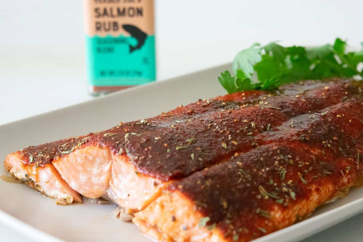 Baked Coho salmon fillet on a rectangular gray plate with parsley with trader joe's salmon rub bottle in the background